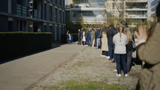 Eine Menschenschlange vor einem Wohnhaus - Die Zuger Kantonalbank hofiert Expats in einem Werbevideo. Nicht zur Freude aller Einheimischen