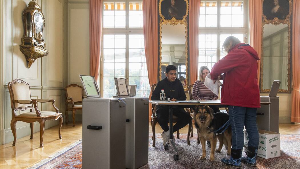 9 Fakten zur Schweizer Demokratie Eine ältere Wählerin gibt in einem historischen Saal ihre Stimme an der Urne ab.