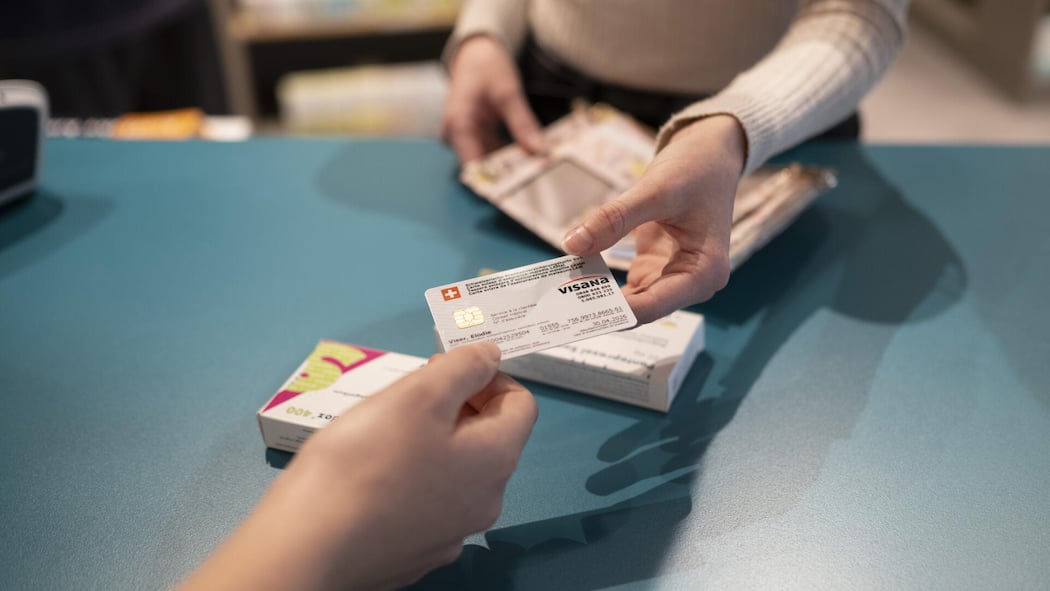 Welche Kantone den Steuerabzug erhöhen und wie Sie profitieren Frau gibt einer anderen Frau die Krankenkassenkarte - Wer profitiert von höheren Steuerabzügen für Krankenkassenprämien? Der Mittelstand oder Gutverdienende? In mehreren Kantonen laufen Initiativen. Ein Überblick