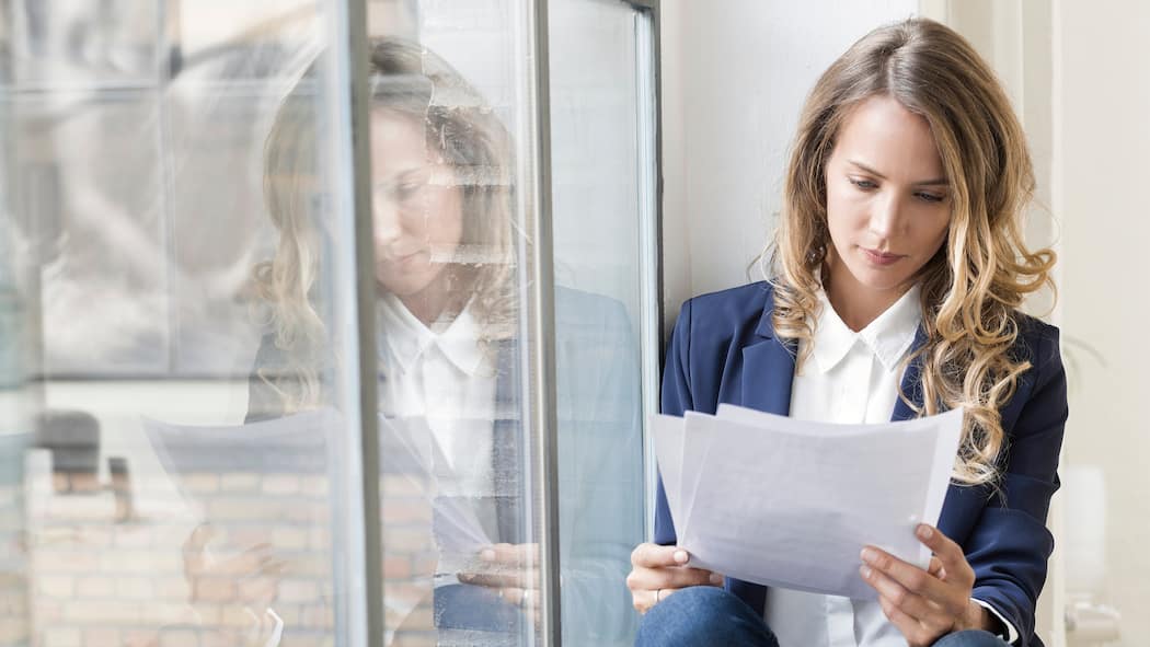 Wie Sie ein Zwischenzeugnis clever begründen Eine Frau sitzt auf dem Fenstersims und liest ihr Zwischenzeugnis durch - Wer vom jetzigen Job weg will, legt für die Stellenbewerbung am besten ein Zwischenzeugnis vor. Doch wie geht man vor, damit die Chefin nichts davon erfährt? Die Tipps des Beobachters.