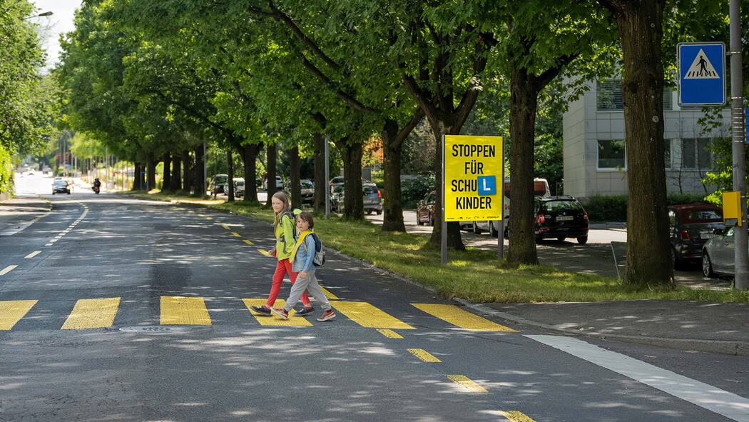 Autofahrer müssen Rücksichtnahme lernen Kinder, die einen Fussgängerstreifen überqueren. Im Hintergrund die Plakatkampagne, die zu mehr Rücksicht aufruft.