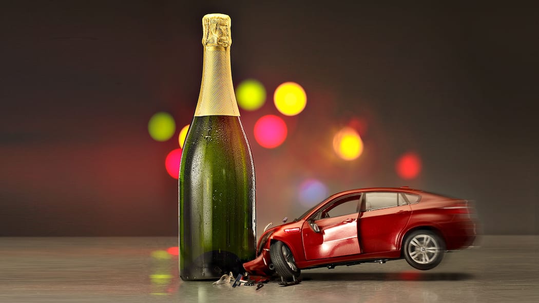 Wie viel Promille liegen drin? Symbolisches Bild in welchem ein Spielzeugauto in eine Sektflasche kracht