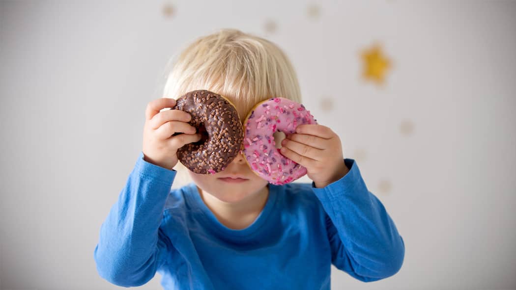 Kinder sollen weniger Werbung für Junkfood sehen Kind hält Donuts vor die Augen - Werbung für besonders süsse, salzige und fettige Produkte an Kinder soll ab 2027 eingeschränkt werden. Noch ist die Regelung aber nicht unter Dach