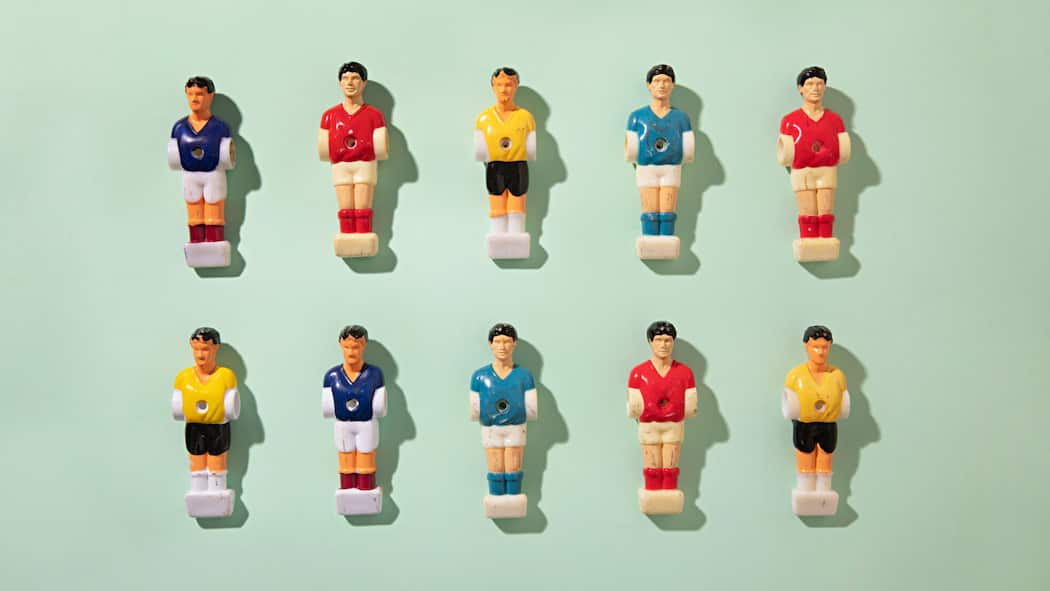 Sind Fussballwetten bei der Arbeit legal? Fussball-Figuren verschiedener Nationen auf einer hellgrünen Oberfläche - Eine Firma organisiert ein Tippspiel, bei dem alle 200 Angestellten mitmachen können. Einsatz: 20 Franken. Ist das erlaubt?