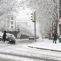 Zu spät im Büro – muss ich länger arbeiten? Eine Person überquert mit einem Kinderwagen die verschneite Strasse in Lausanne. Müssen Arbeitnehmerinnen und Arbeitnehmer länger arbeiten, wenn sie wegen des Schnees und vereister Strassen zu spät zur Arbeit kommen?