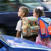 Der lange Kampf um sichere Schulwege Zwei Schulkinder stehen an der Strasse und wollen diese überqueren.