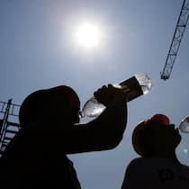 Wer hat hitzefrei in der Schweiz? Zwei Bauarbeiter trinken aus Wasserflaschen. Hohe Temperaturen machen die Arbeit beschwerlich. Wer kann hitzefrei machen? Eine Übersicht.