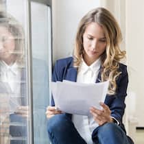 Wie Sie ein Zwischenzeugnis clever begründen Eine Frau sitzt auf dem Fenstersims und liest ihr Zwischenzeugnis durch - Wer vom jetzigen Job weg will, legt für die Stellenbewerbung am besten ein Zwischenzeugnis vor. Doch wie geht man vor, damit die Chefin nichts davon erfährt? Die Tipps des Beobachters.