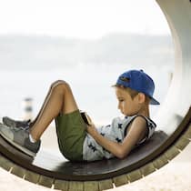 Wie weit sollen Eltern das Handy überwachen? Ein kleiner Junge auf einem Spielplatz hat seinen Blick auf ein Smartphone vertieft.