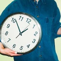 Ausstempeln zum Rauchen? Das muss sein – eigentlich Eine Person mit Kaffeetasse in einer Hand und einer Wanduhr in der anderen Hand vor grünem Hintergrund. Wie Arbeitspausen in der Schweiz geregelt sind, legt das Arbeitsgesetz klar fest.