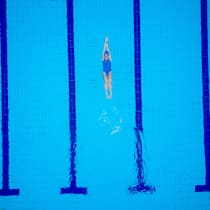 Stiftung zahlt den Schwimmverein Female swimmer on evening training on swimming pool, warming up, swimming backstroke during training.