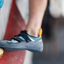 Dank Spenden kann er Freundschaften pflegen im Kletterverein Detail of a climber's shoe firmly placed on a hold on an indoor climbing wall, showcasing grip and technique in a sport environment.