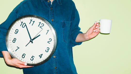 Eine Person mit Kaffeetasse in einer Hand und einer Wanduhr in der anderen Hand vor grünem Hintergrund. Wie Arbeitspausen in der Schweiz geregelt sind, legt das Arbeitsgesetz klar fest.