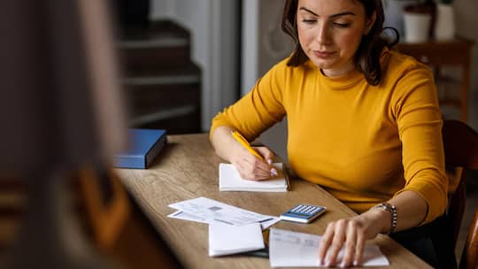 Selective focus shot of worried young woman sitting at her home office desk, sorting out her monthly bills and expenses and struggling with finances.