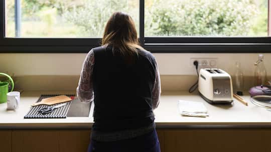 Woman standing with her back to the camera, washing dishes in a modern kitchen sink, looking thoughtful
2252619927